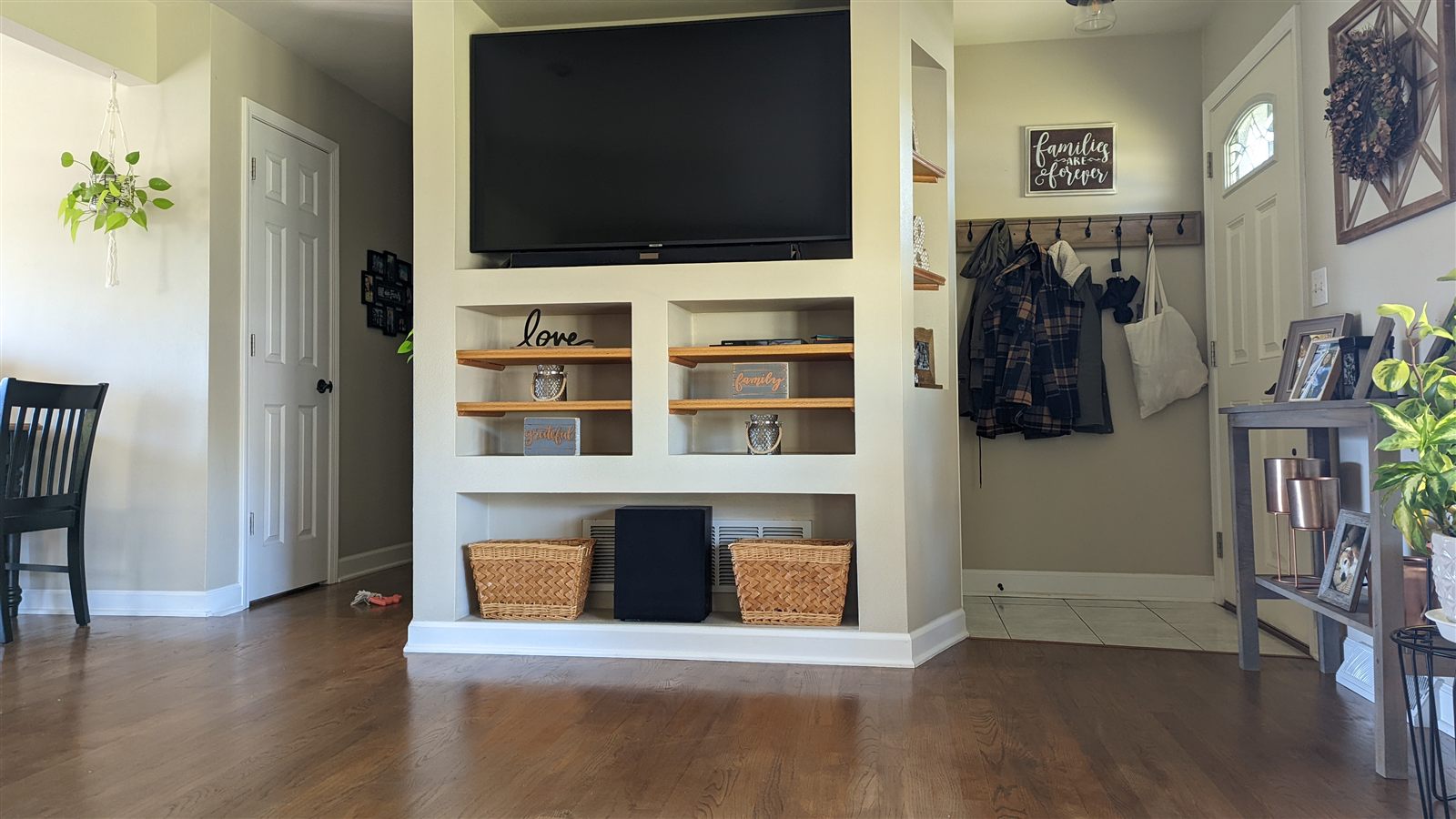 Custom built-in entertainment center with oak shelving and entryway coat rack, finished in white with hardwood floors